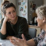 Parent et enfant adulte échangent un moment tendre et complice, se regardant avec une compréhension mutuelle et bienveillante, illustrant la transformation silencieuse de leur relation.