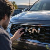 Gros plan sur le logo minimaliste anguleux et stylisé de Kia gravé sur la calandre d'une voiture moderne, aux lettres fusionnées créant l'illusion d'un « KN ».